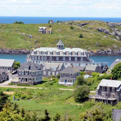 A large building and houses on a green hillside next to water